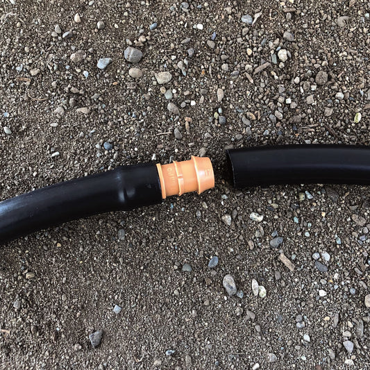 A brown 1/2" barbed drip tube coupler fitting connected to 1/2" drip tubing with soil in the background.