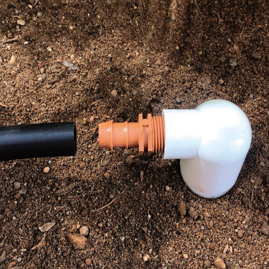 A brown barbed 1/2" drip tube adapter with a 1/2 inch male pipe thread (MPT) with soil in the background.