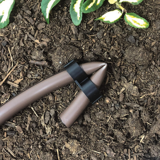 A black Figure-8 end plug for 1/2 inch drip tubing with plants and soil in the background.