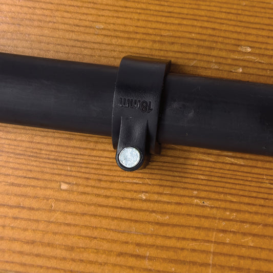 A black plastic U-shaped drip tube mounting clamp with a metal nail for securing. Drip tube clamp is displayed attached to wood surface in the background.