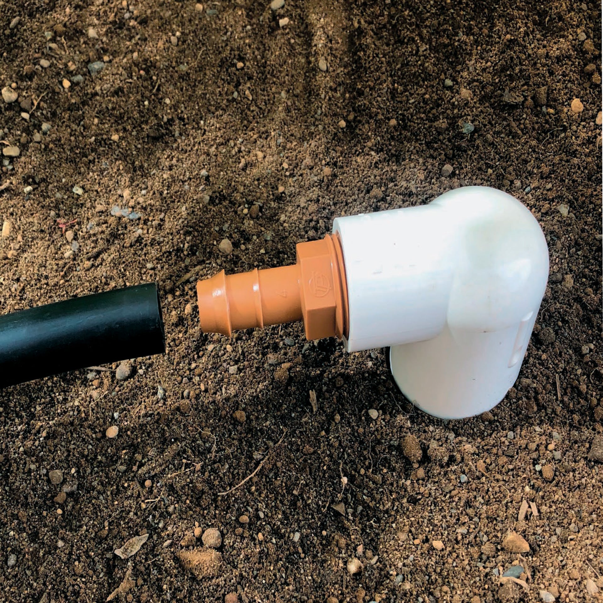A brown barbed drip tube adapter with a 3/4-inch threaded connection connected to 1/2" drip tubing with soil in the background.