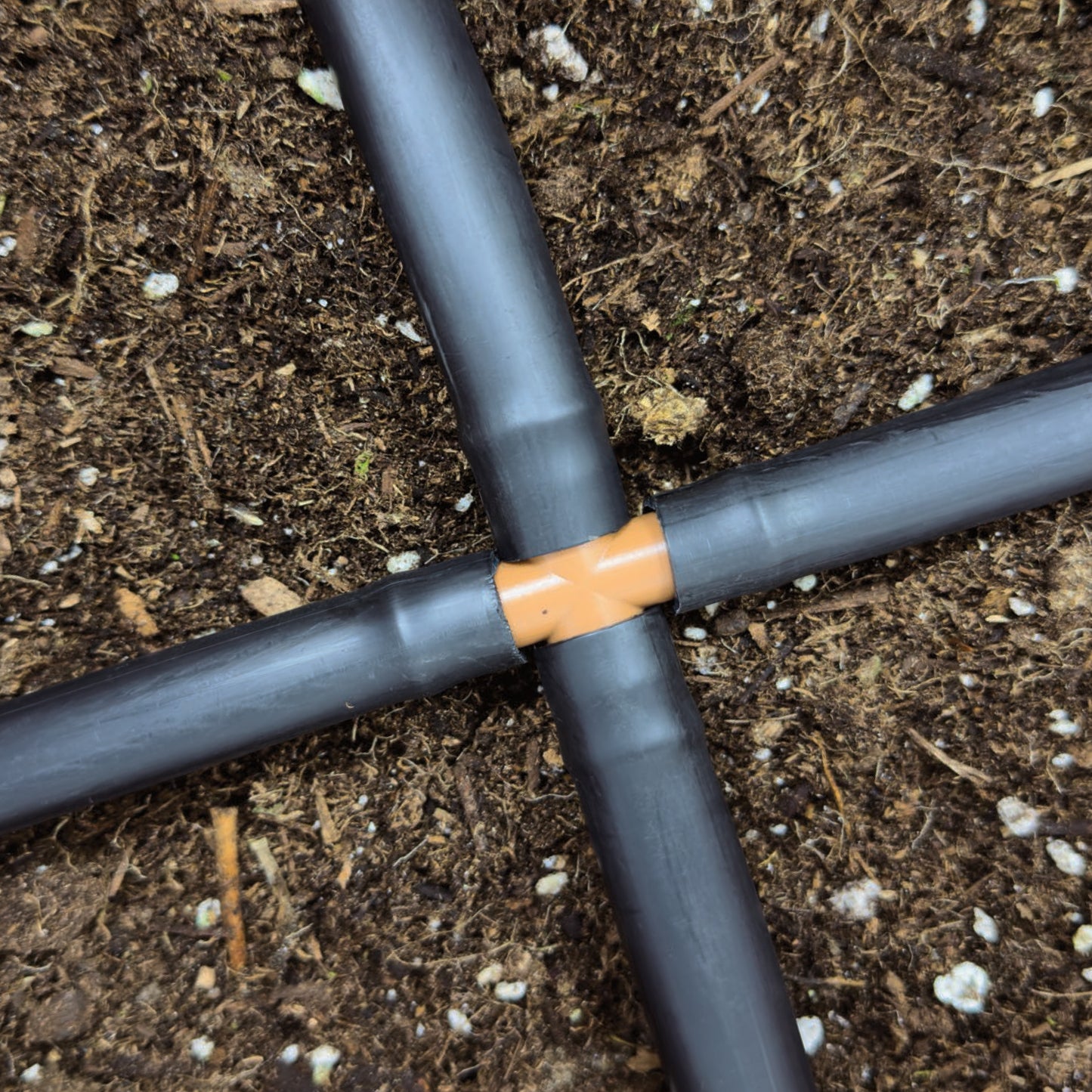 A brown barbed drip tube cross connected to 1/2" drip tubing with soil in the background.