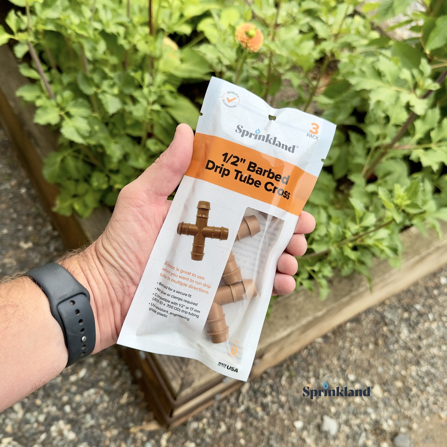A 3 pack of 1/2" brown barbed drip tube cross with plants and soil in the background.